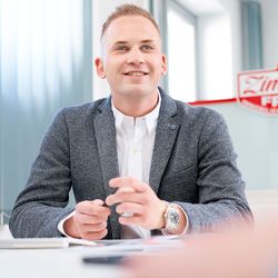 Dennis Zimmer, Inhaber von Zimmer FREI! Real Estate, sitzt an einem Schreibtisch im Flensburger Büro und spricht mit einem Kunden.