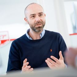 Denis Stein von Zimmer FREI! Real Estate Hamburg sitzt ein einem Schreibtisch und erklärt etwas.