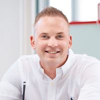 Dennis Zimmer, Inhaber von Zimmer FREI! Real Estate, sitzt an seinem Schreibtisch im Flensburger Büro und lächelt.